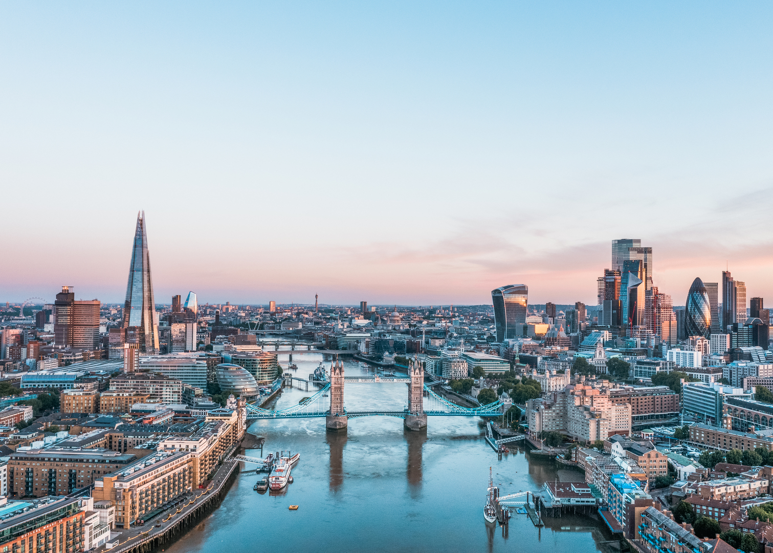 Elevated view of the London skyline at sunrise, featuring the Tower Bridge and The Shard.