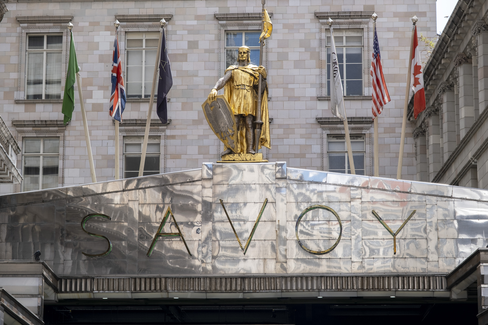 The Savoy Hotel entrance in London, featuring a golden statue and the hotel's name in Art Deco lettering.