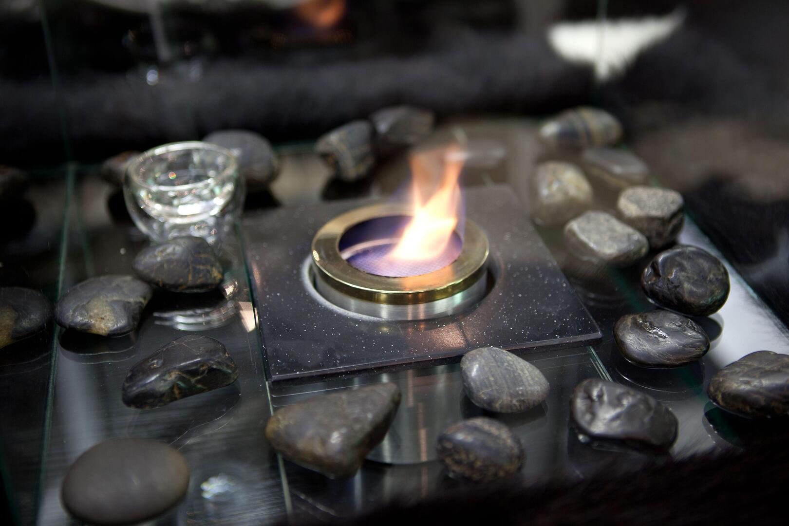 Bioethanol fireplace burning on a glass surface surrounded by stones.
